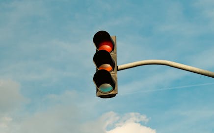 A traffic light with red signal set against a blue sky, signifying stop in urban streets.