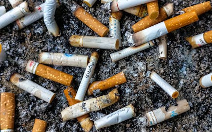 Close-up image of numerous cigarette butts and ash in an ashtray, highlighting smoking issues.