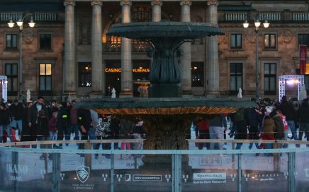 Evening view of Kurhaus Wiesbaden with people gathered around a fountain in winter.