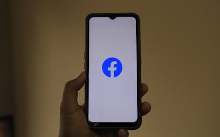 A smartphone held in hand showing the Facebook logo on its screen.