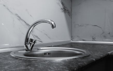 A stylish stainless steel kitchen faucet with a sleek and modern design set against a marble backsplash.