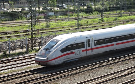 An ICE train speeding down the tracks on a sunny day with greenery in the background.