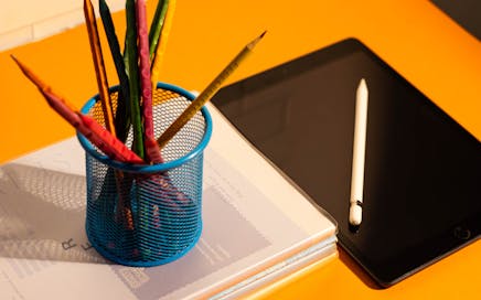 Bright flat lay of pencils and tablet on an orange desk, perfect for school or office scenes.