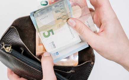 Close-up of hands handling euro bills with a wallet, depicting financial transactions.