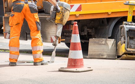 Construction worker using jackhammer beside traffic cone on urban street