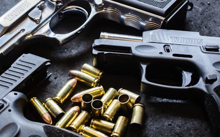 Detailed shot of various handguns and bullets arranged on a textured dark surface, showcasing firearm elements.