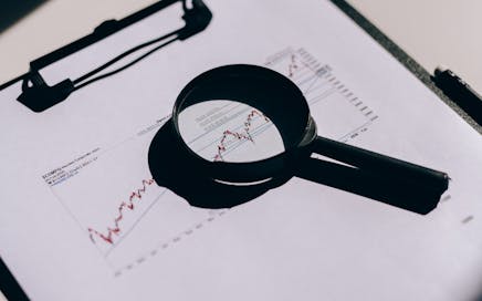 Detailed close-up of financial documents with graphs and magnifying glass on a clipboard.