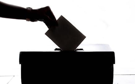 Silhouette of a hand placing a vote into a ballot box, symbolizing democracy.
